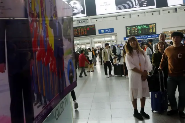 Commuters watch on a big screen in Seoul's train station