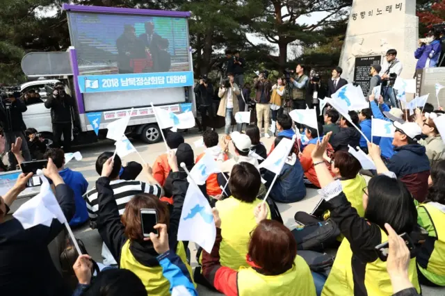 People wave flags in front of a TV screen in Paju, South Korea