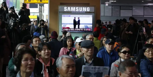 Commuters watch on a big screen in Seoul's train station