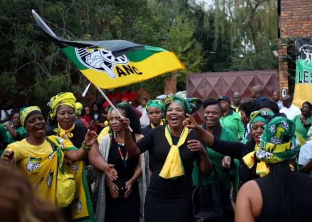 Women sing and wave flags outside the Soweto home