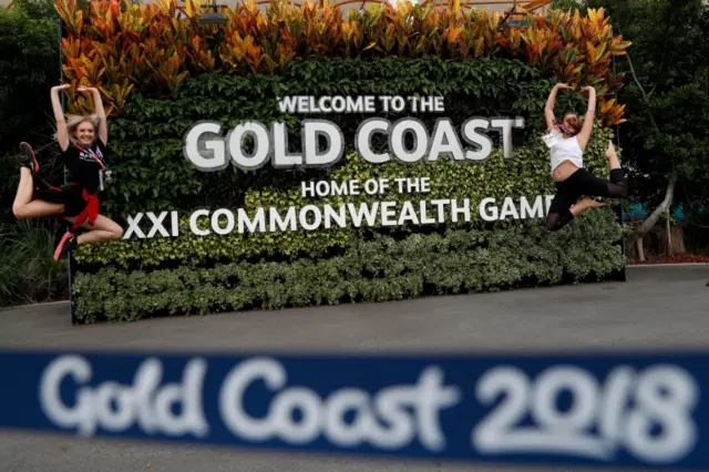 Two dancers jump next to a Commonwealth Games sign