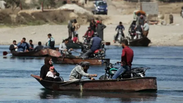 People cross the Euphrates River on boats in Raqqa, Syria