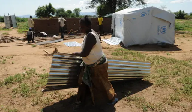 A newly arrived refugee woman, carries a sheet of roofing material outside her tent as other refugees work in the background, at Kakuma refugee camp, North-Western Kenya on September 6, 2010.