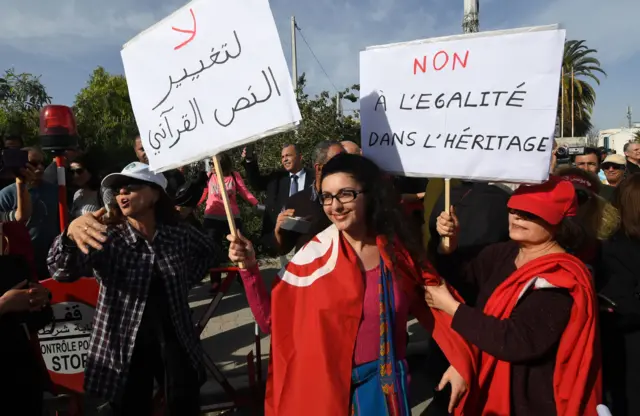 Two Tunisian women holding placards with slogans against altering religious law concerning inheritance, confront other protesters calling for equality on March 10, 2018, in the capital Tunis.