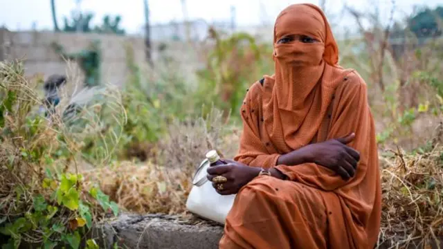 A woman sits down holding a bottle of cough syrup