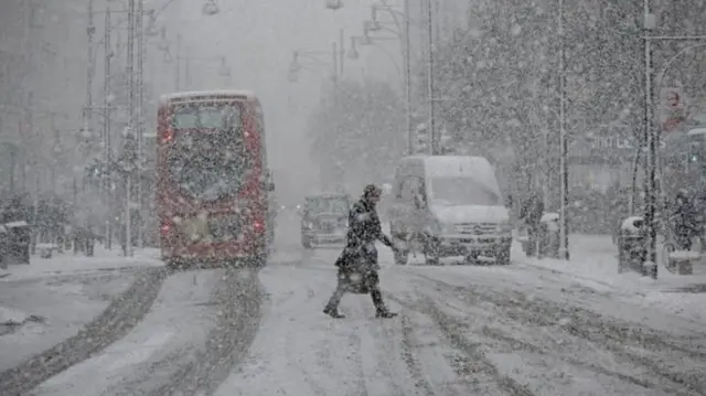 A man walks across a snow-covered street in London