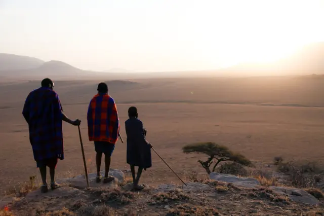 Maasai cattle herder, Parakapooni, and his brother and son look over the brown plains of the Serengeti, Tanzania.