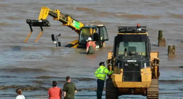 Workers trying to rescue the stranded JCB.