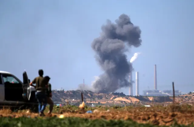 Palestinians look at smoke billowing from the site of an Israeli air strike in Beit Lahia (14 May 2018)