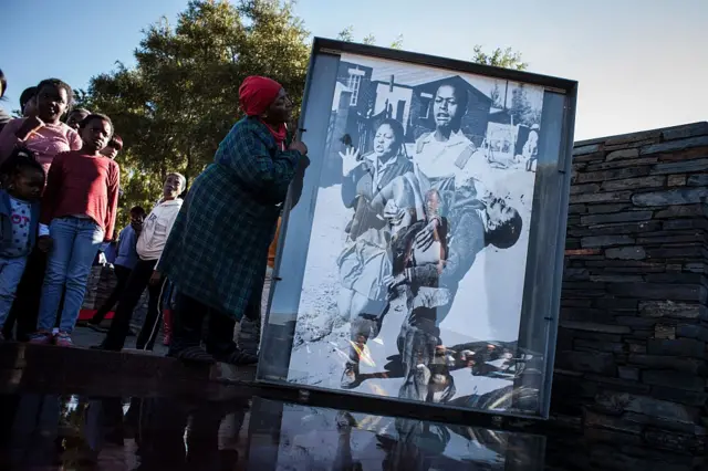 A woman stands next to the iconic photograph by Sam Nzima showing Hector Pieterson carried away during the start of the Soweto Uprising in 1976, during celebrations to commemorate the 40th anniversary of the day