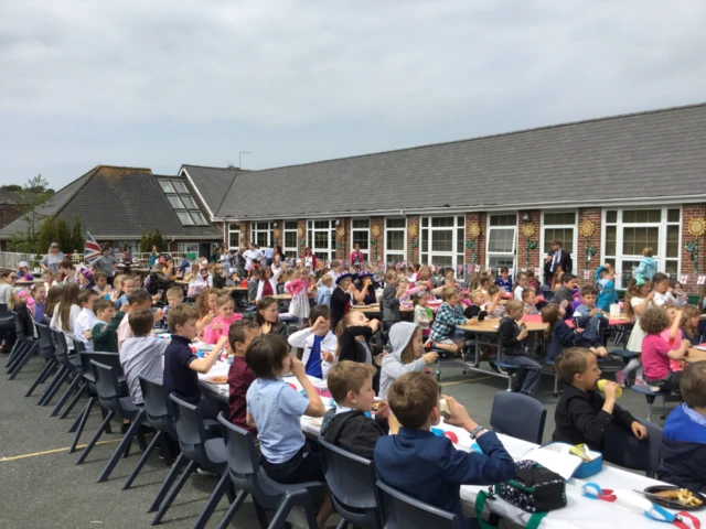 hundreds of children sitting at tables outside a school building