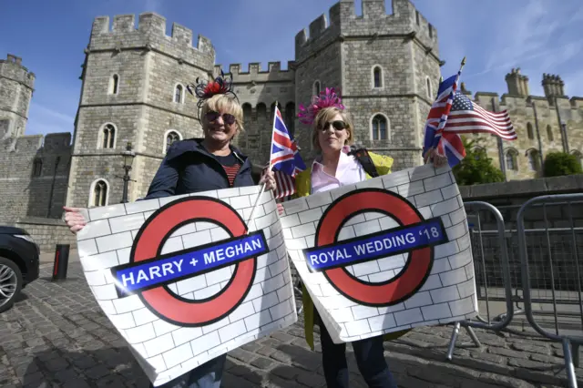 Two women holding Harry and Meghan London Underground signs