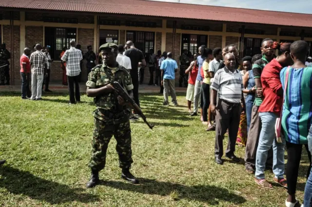 A security guard stands next to voters queuing to vote outside a polling station in Bujumbura, on 17 May 2018 during a referendum on constitutional reforms