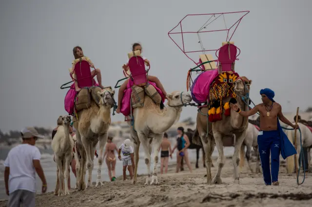 Tourists take camel rides on the beach on June 30, 2016 in Djerba, Tunisia.