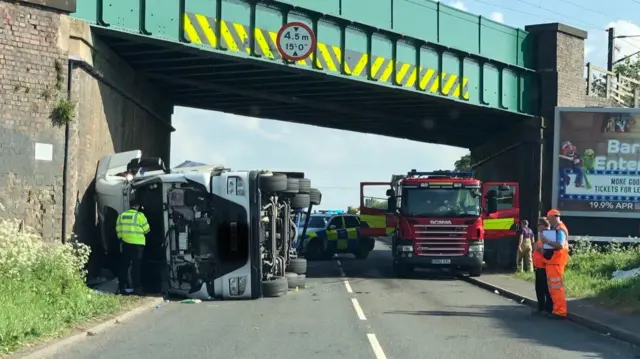 The lorry on its side under bridge