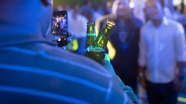 A man holds two bottles of beer as he takes a picture