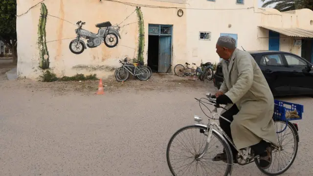 In Tunisia, a man rides his bicycle leisurely past graffiti in the resort island of Djerba.