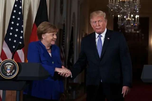 Merkel (left) shakes hands with Trump