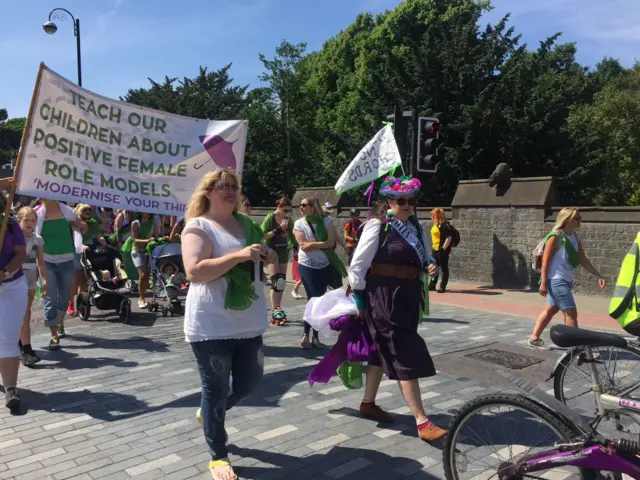 Marchers approaching Cardiff Castle with banner saying 'Teach our children about positive female role models'