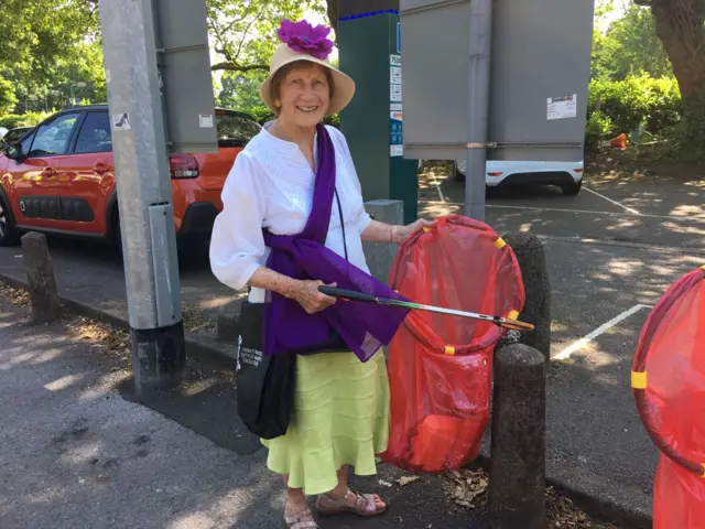 Image of Alma Thomas in a violet scarf with a red bin bag collecting litter