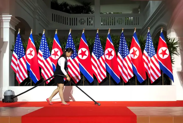 A worker vacuums the stage at the spot where U.S. President Donald Trump and North Korea"s leader Kim Jong Un are expected to meet and shake hands for the first time at the start of their summit at the Capella Hotel