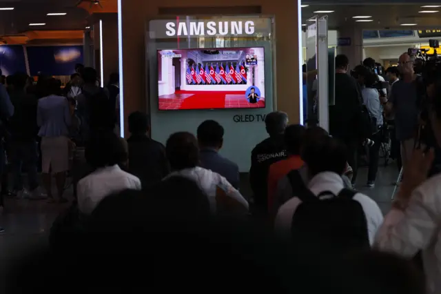 South Koreans watch a TV screen displaying a broadcast of the historic meeting