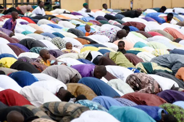 Children sit between Muslims praying at the site of a bus terminal in Adjame, a quarter of Abidjan, on June 14, 2018, as the Holy Month of Ramadan is about to end in Ivory Coast.