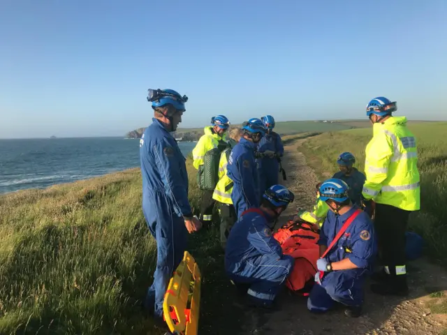 team of medics helping a person on the floor of a coastal path