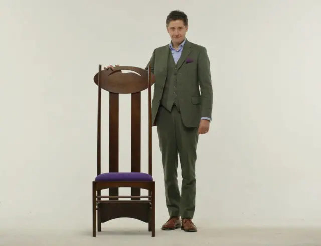 Lachlan Goudie presented a documentary to mark Mackintosh's 150th anniversary. Here he is with a famous Mackintosh high-backed chair.