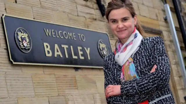 Jo Cox by a sign welcoming people to Batley