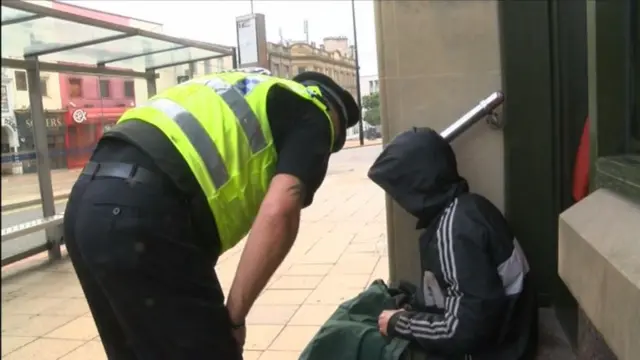 Police officer speaks to a man wearing a hood