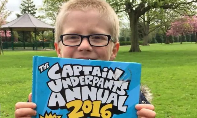 A child stood in a park  holding a book.