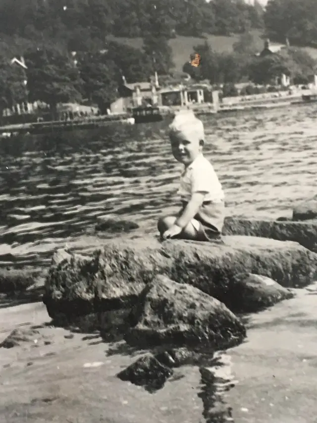 Keith as a child sat on a rock by some water