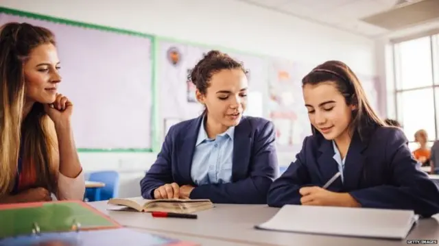 Two children working in school as their teacher looks on