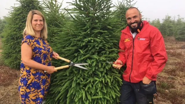 Two people stand side-by-side of a Christmas tree