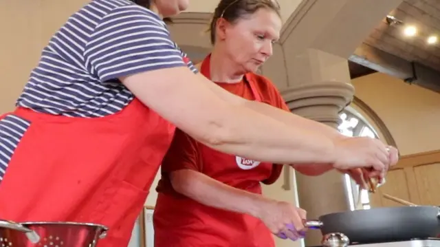 Two women make food in a pan