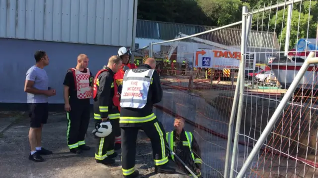 firefighters chatting with fire engines and large commercial unit in background