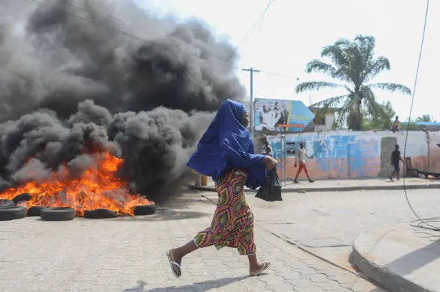 Girl running past burning tyres during an anti-government protest in Benin - March 2018