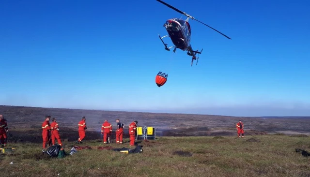 A helicopter brings water to fire crews on Saddleworth Moor.