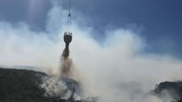 A helicopter doses flames on moorland.