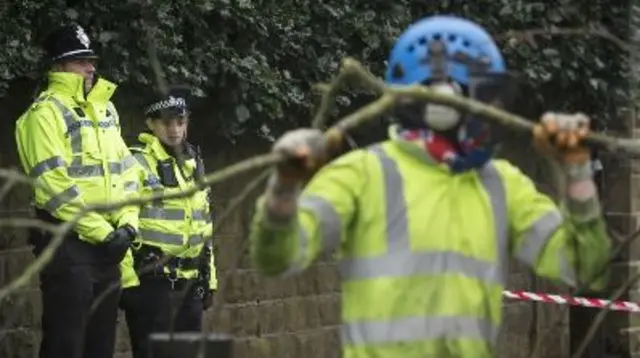 Police officers look on as workers remove tree branches