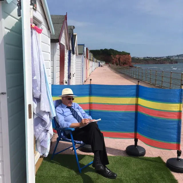 man on deck chair outside a beach hut