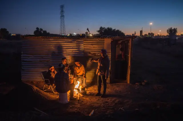 Independent miners, formerly illegal miners, sit around a fire as they spend the night in their corrugated iron quarters on June 5, 2018 in Kimberly, Northern Cape, South Africa.