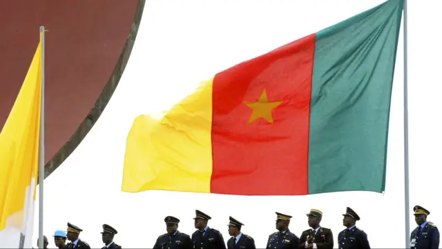 Military personnel stand under Cameroon's national flag