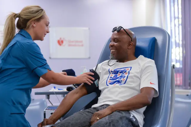 A man wearing an England shirt gives blood