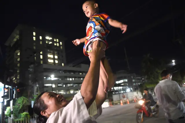 A woman lifts her child near the hospital, seen at left, as ambulance transporting members of the children"s football team arrives in the northern Thai city of Chiang Rai on July 10, 2018