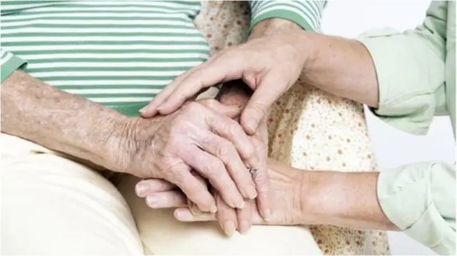 Two people holding hands one of them is an older person.