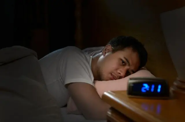 A man in bed with an alarm clock.