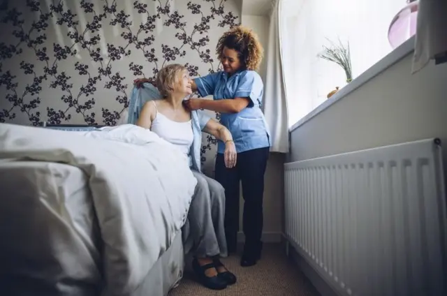 A care worker helping to dress an elderly woman.