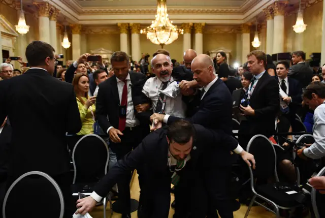 A man is escorted out of the room after displaying a placard reading "nuclear weapons ban treaty"